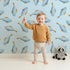 Lovely child standing in front of Whimsy Tots Little Swimmer Fish Wallpaper in Blue with fish in design.