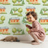 Lovely child standing in front of Whimsy Tots Cottage Garden Village Wallpaper in Mint Green with tree, bush, house in design.