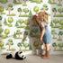 Lovely child standing in front of Whimsy Tots Forest Meadow Grove Wallpaper in White with tree, bush in design.
