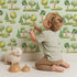 Lovely child standing in front of Whimsy Tots Forest Meadow Grove Wallpaper in Mint Green with tree, bush in design.