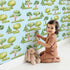Lovely child standing in front of Whimsy Tots Forest Meadow Grove Wallpaper in Blue with tree, bush in design.