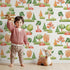 Lovely child standing in front of Whimsy Tots Autumn Meadow Grove Wallpaper in White with tree, bush in design.