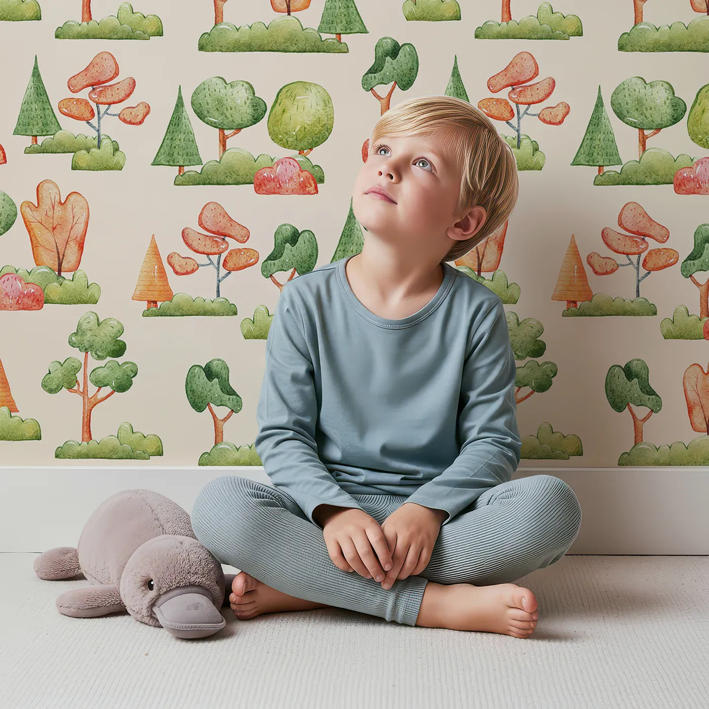 Lovely child standing in front of Whimsy Tots Autumn Meadow Grove Wallpaper in Cream with tree, bush in design.