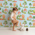 Lovely child standing in front of Whimsy Tots Autumn Meadow Grove Wallpaper in Blue with tree, bush in design.