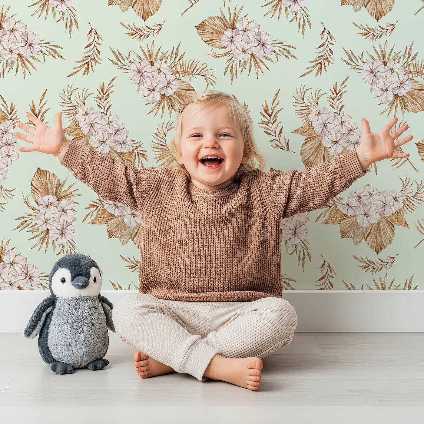 Lovely child standing in front of Whimsy Tots Dried Bloom Cascade Wallpaper in Mint Green with flower, palm, leaf in design.