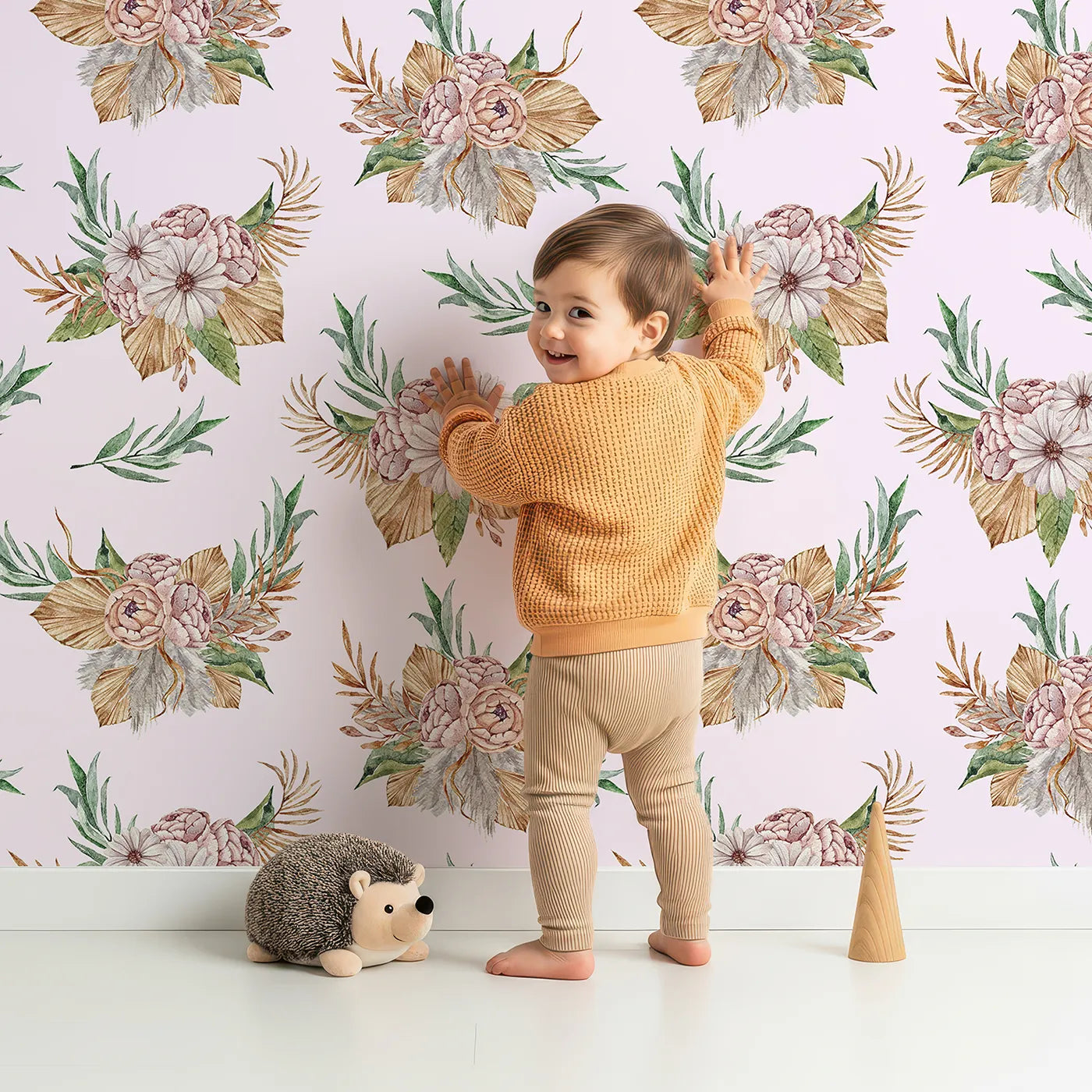 Lovely child standing in front of Whimsy Tots Rustic Blush Bouquet Wallpaper in Pink with flower, leaf, palm in design.