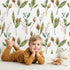 Lovely child standing in front of Whimsy Tots Woodland Forage Sprigs Wallpaper in White with leaf, pod, sprig in design.