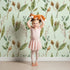 Lovely child standing in front of Whimsy Tots Woodland Forage Sprigs Wallpaper in Mint Green with leaf, pod, sprig in design.