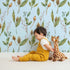 Lovely child standing in front of Whimsy Tots Woodland Forage Sprigs Wallpaper in Blue with leaf, pod, sprig in design.
