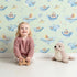 Lovely child standing in front of Whimsy Tots Whale Submarine Adventure Wallpaper in Mint Green with whale, submarine, fish, anchor, octopus, bunting in design.