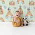 Lovely child standing in front of Whimsy Tots Rainbow Castle Dreams Wallpaper in Mint Green with castle, rainbow, moon, cloud, star, net in design.