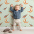 Lovely child standing in front of Whimsy Tots Moon Perch Birds Wallpaper in Mint Green with bird, moon in design.
