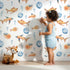 Lovely child standing in front of Whimsy Tots Undersea Bubble Friends Wallpaper in White with fish, bubble, shell in design.