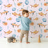 Lovely child standing in front of Whimsy Tots Undersea Bubble Friends Wallpaper in Pink with fish, bubble, shell in design.