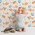 Lovely child standing in front of Whimsy Tots Undersea Bubble Friends Wallpaper in Beige with fish, bubble, shell in design.