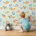 Lovely child standing in front of Whimsy Tots Undersea Bubble Friends Wallpaper in Mint Green with fish, bubble, shell in design.