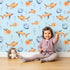 Lovely child standing in front of Whimsy Tots Undersea Bubble Friends Wallpaper in Blue with fish, bubble, shell in design.