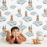 Lovely child standing in front of Whimsy Tots Castle Cloud Drift Wallpaper in White with castle, cloud, moon in design.