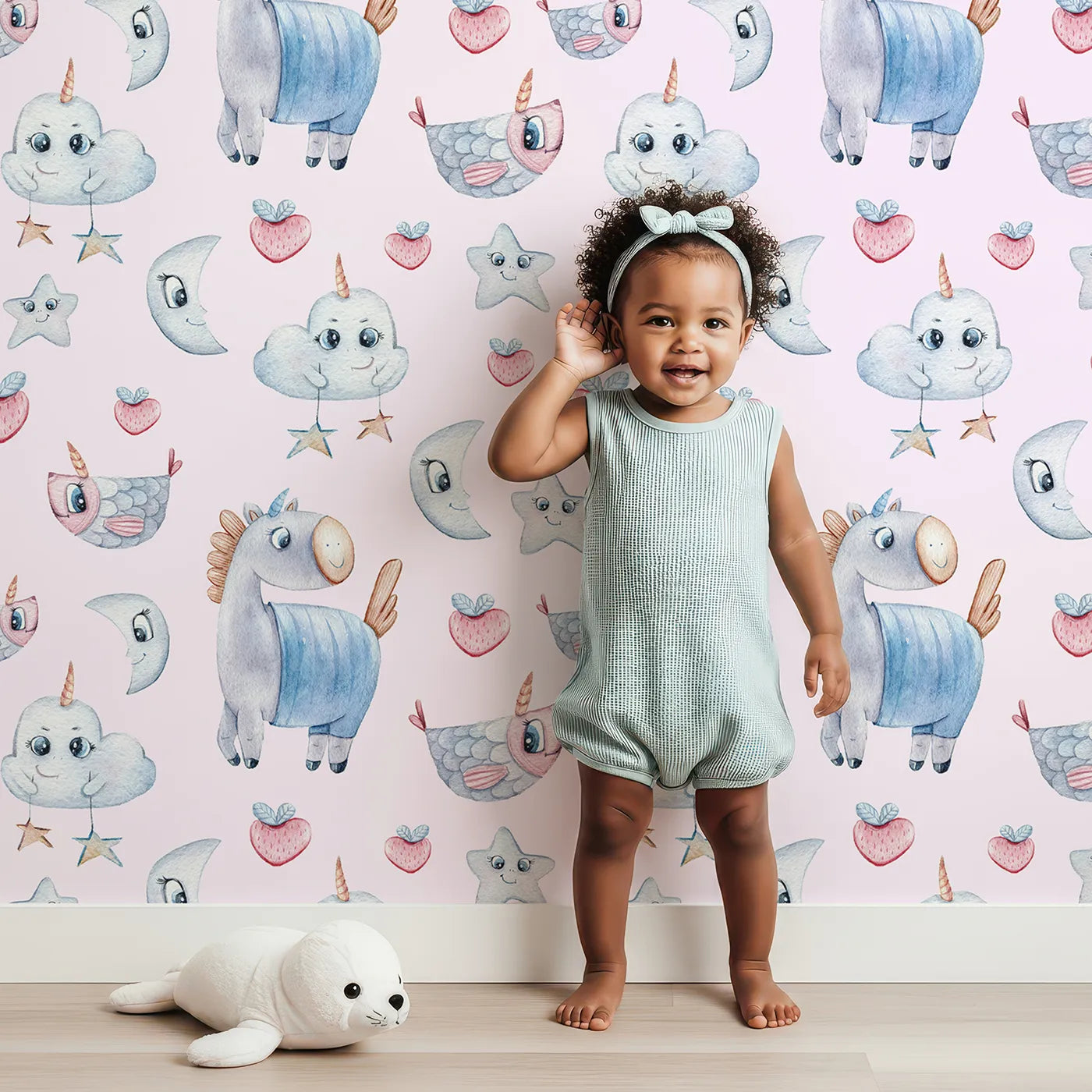 Lovely child standing in front of Whimsy Tots Starlight Narwhal Parade Wallpaper in Pink with narwhal, unicorn, moon, star, cloud, heart, fruit in design.