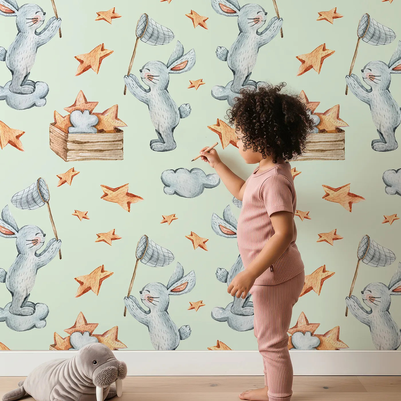 Lovely child standing in front of Whimsy Tots Star Catcher Bunnies Wallpaper in Green with rabbit, star, cloud, net in design.
