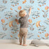 Lovely child standing in front of Whimsy Tots Moonlight Bunny Dreams Wallpaper in Blue with rabbit, balloon, moon, star, cloud in design.