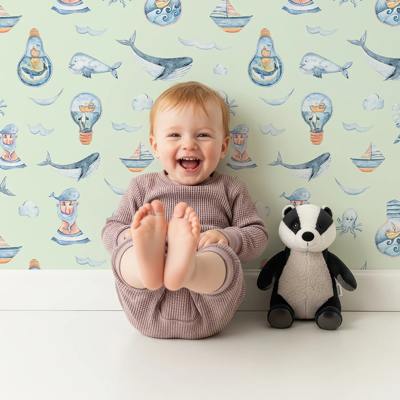 Lovely child standing in front of Whimsy Tots Maritime Whimsy Wallpaper in Mint Green with whale, octopus, boat, sailor, cloud, bulb, bottle in design.
