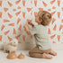 Lovely child standing in front of Whimsy Tots Scattered Heart Sprinkles Wallpaper in White with heart, brushstroke, splash in design.