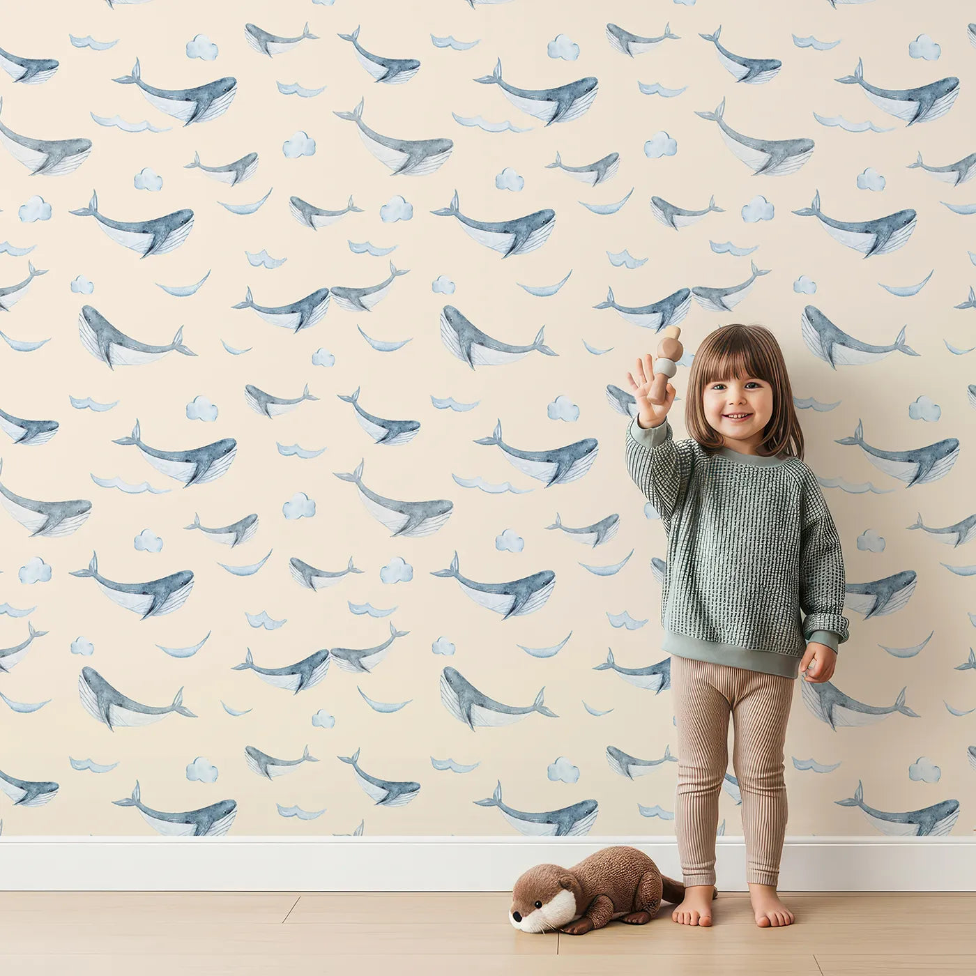 Lovely child standing in front of Whimsy Tots Whale Cloud Voyage Wallpaper in Beige with whale, cloud, splash in design.
