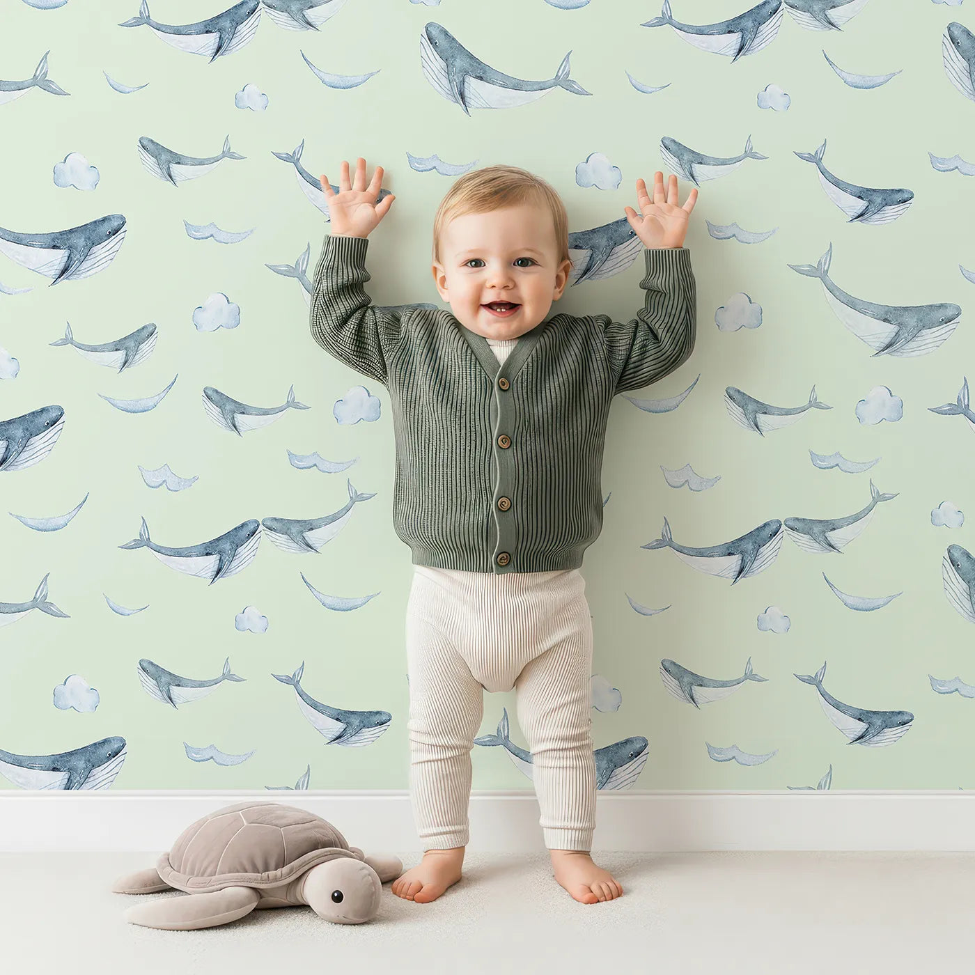 Lovely child standing in front of Whimsy Tots Whale Cloud Voyage Wallpaper in Mint Green with whale, cloud, splash in design.