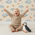 Lovely child standing in front of Whimsy Tots Cloudy Star Drift Wallpaper in Beige with star, cloud in design.