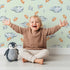Lovely child standing in front of Whimsy Tots Cloudy Star Drift Wallpaper in Mint Green with star, cloud in design.