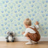Lovely child standing in front of Whimsy Tots Blue Hearts Wallpaper in Mint with heart, outline, watercolor in design.