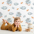 Lovely child standing in front of Whimsy Tots Bunny Cloud Dreams Wallpaper in White with bunny, cloud, star, string, moon in design.