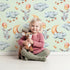 Lovely child standing in front of Whimsy Tots Starry Bunny Balloons Wallpaper in Mint Green with bunny, balloon, star, cloud, moon in design.