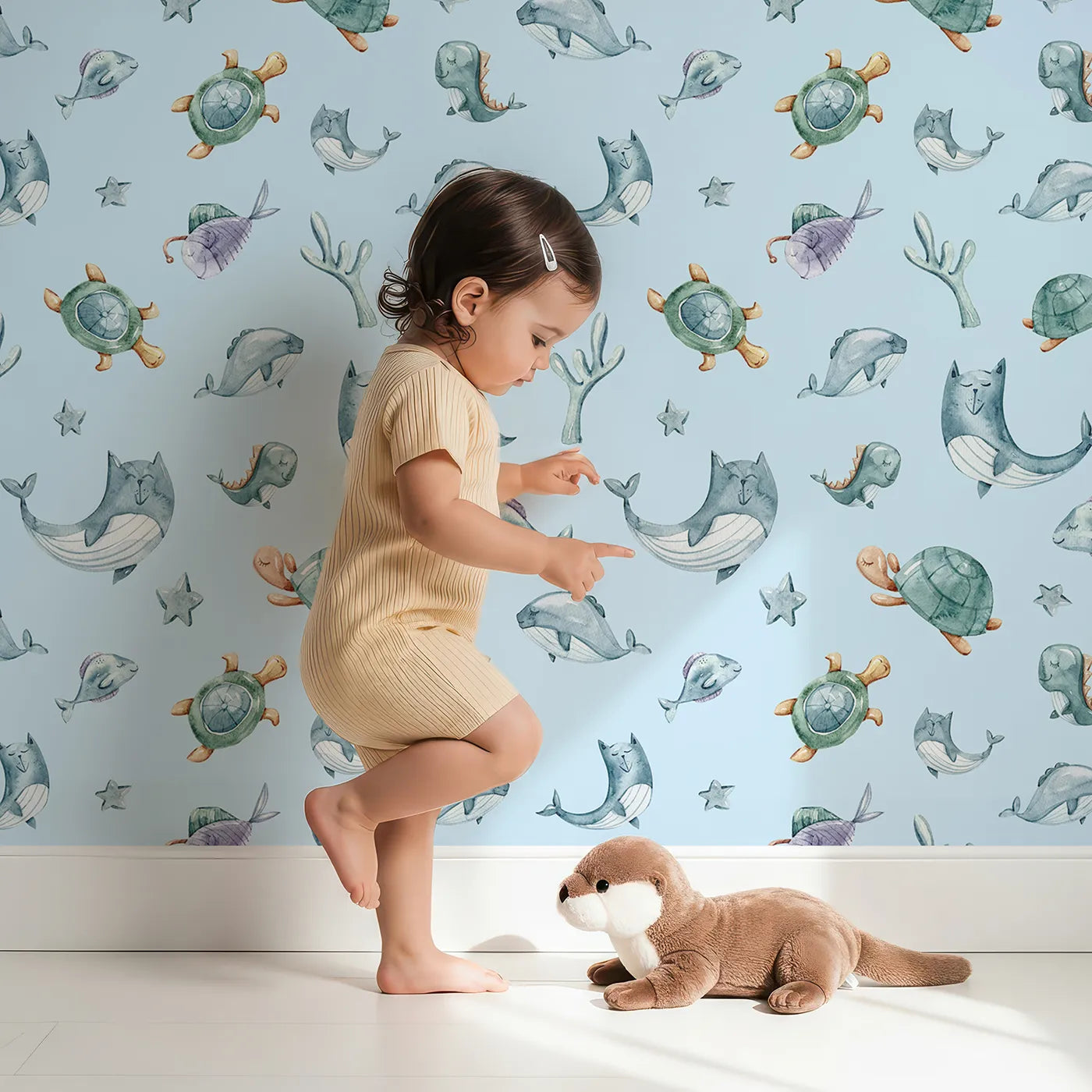 Lovely child standing in front of Whimsy Tots Gentle Sea Friends Wallpaper in Sky Blue with whale, turtle, dolphin, fish, coral, seashell, seaweed, star in design.