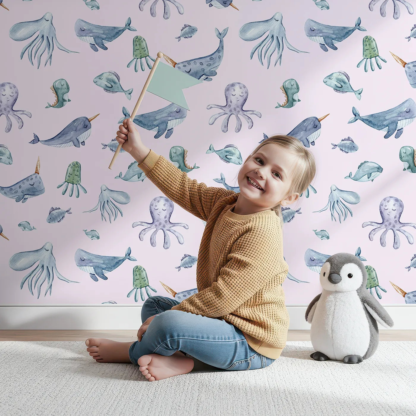 Lovely child standing in front of Whimsy Tots Gentle Ocean Parade Wallpaper in Pink with whale, narwhal, octopus, jellyfish, fish in design.