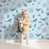 Lovely child standing in front of Whimsy Tots Gentle Ocean Parade Wallpaper in Sky Blue with whale, narwhal, octopus, jellyfish, fish in design.