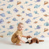 Lovely child standing in front of Whimsy Tots Dreamy Fish Parade Wallpaper in Peach with fish, fin, puffer, anglerfish, goby in design.