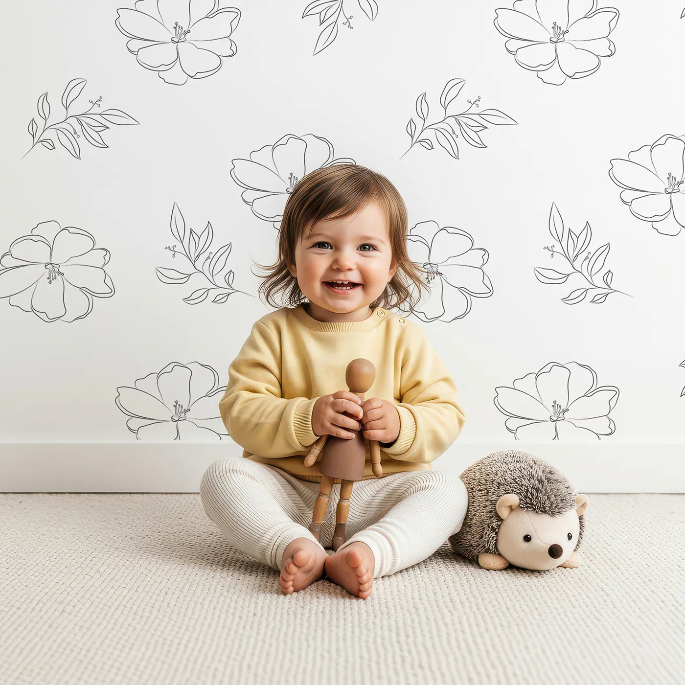 Lovely child standing in front of Whimsy Tots Line Art Camellia Wallpaper in White with flower, camellia, lineart, leaf in design.