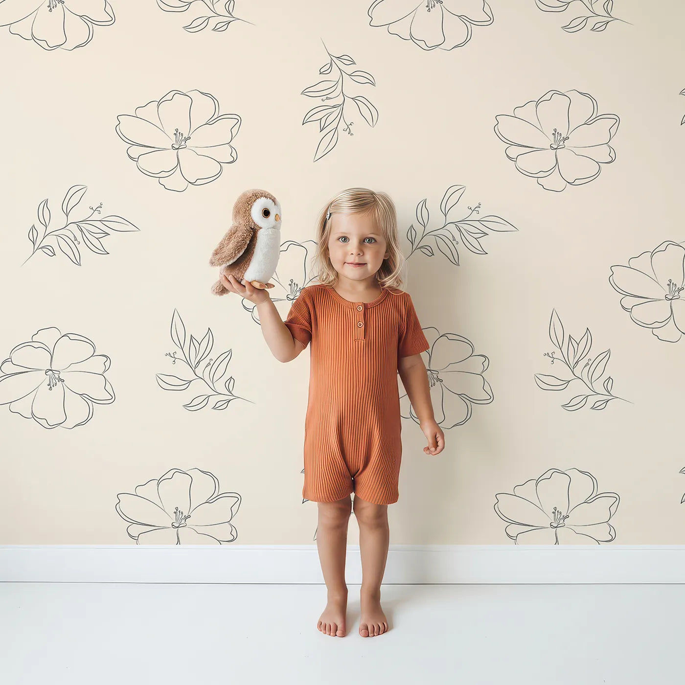 Lovely child standing in front of Whimsy Tots Line Art Camellia Wallpaper in Cream with flower, camellia, lineart, leaf in design.