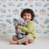 Lovely child standing in front of Whimsy Tots Counting Cloud Sheep Wallpaper in White with cloud, sheep, star, mobile in design.