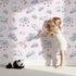 Lovely child standing in front of Whimsy Tots Counting Cloud Sheep Wallpaper in Blush Pink with cloud, sheep, star, mobile in design.