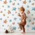 Lovely child standing in front of Whimsy Tots Starry Drift Wallpaper in White with star, watercolor, sky, night in design.