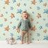 Lovely child standing in front of Whimsy Tots Starry Drift Wallpaper in Mint Green with star, watercolor, sky, night in design.
