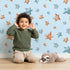 Lovely child standing in front of Whimsy Tots Starry Drift Wallpaper in Blue with star, watercolor, sky, night in design.