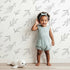 Lovely child standing in front of Whimsy Tots Line Art Leaf Dance Wallpaper in White with leaf, branch, botanical, outline in design.