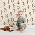 Lovely child standing in front of Whimsy Tots Botanical Numbers Grid in Sand with number, leaf, branch, stem in design.