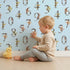 Lovely child standing in front of Whimsy Tots Botanical Numbers Grid in Blue with number, leaf, branch, stem in design.