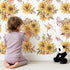 Lovely child standing in front of Whimsy Tots Sun-Kissed Meadow Blooms Wallpaper with sunflower, flower, leaf, bouquet in design.