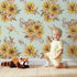 Lovely child standing in front of Whimsy Tots Sun-Kissed Meadow Blooms in Mint Green with sunflower, flower, leaf, bouquet in design.